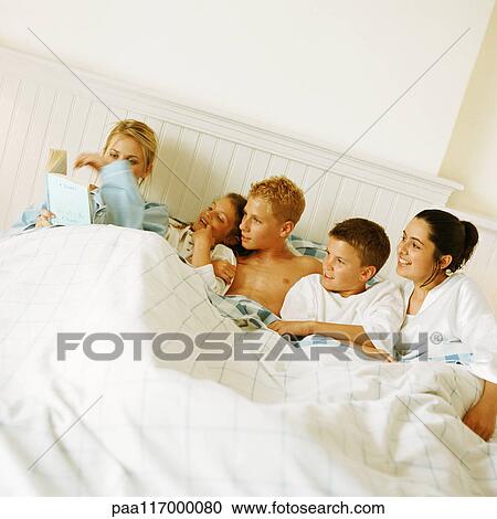 Stock Image - Young people lying in bed, one reading. Fotosearch