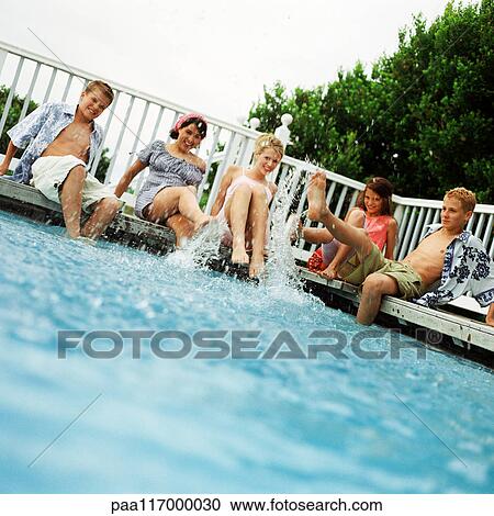 Young people sitting around swimming pool, splashing feet in water View Large Photo Image Stock Image - Young people sitting around swimming pool, splashing feet in water. Fotosearch