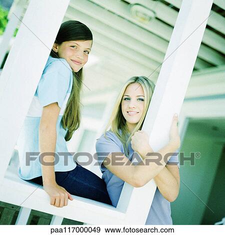 Stock Photo - Young woman and girl leaning against posts on porch. Fotosearch