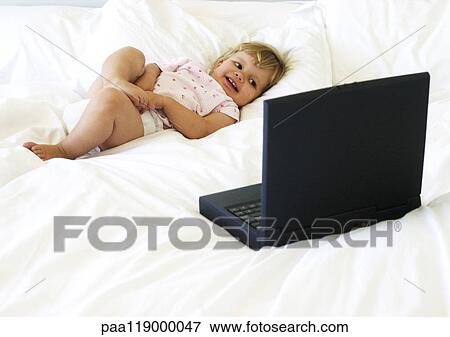 Baby lying on bed, looking at laptop computer View Large Photo Image Stock Photo - Baby lying on bed, looking at laptop computer. Fotosearch