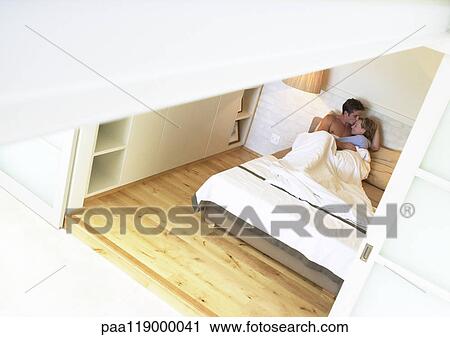 Stock Image - Couple in bed, embracing, high angle view. Fotosearch