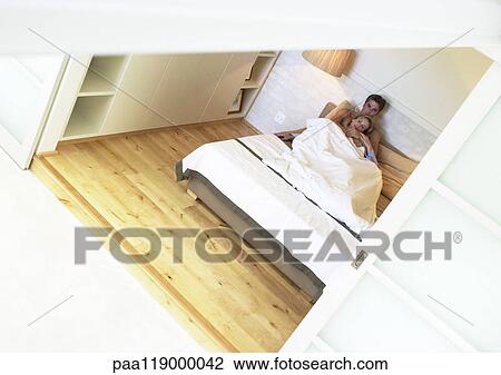 Stock Image - Couple lying together in bed, high angle view. Fotosearch