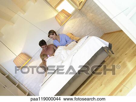 Picture - Couple sitting in bed with baby. Fotosearch