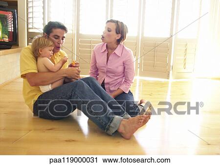 Stock Image - Couple sitting on floor, man holding baby. Fotosearch