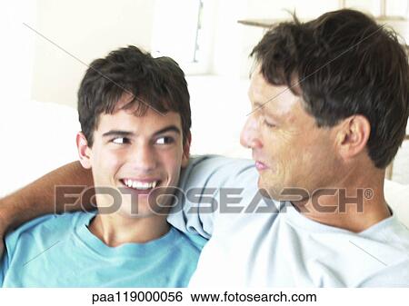 Stock Photograph - Father and teenage boy smiling at each other, man's arm around boy. Fotosearch