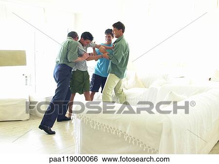 Stock Photograph - Grandfather, father and boys standing in living room, playfighting. Fotosearch