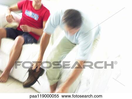 Stock Photography - Man leaning forward, holding shoe, teenage boy sitting on sofa, blurred. Fotosearch