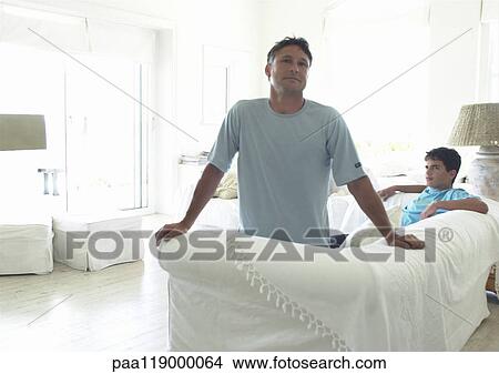 Picture - Man on teenage boy in living room, man looking at camera. Fotosearch