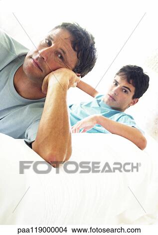 Mature man and teenage boy sitting on sofa View Large Photo Image Picture - Mature man and teenage boy sitting on sofa. Fotosearch