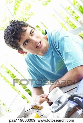 Stock Photo - Teenage boy having breakfast outside, portrait. Fotosearch