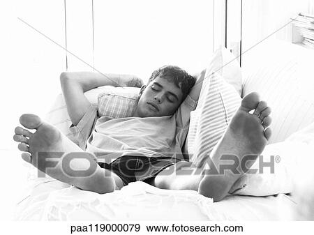 Stock Photo - Teenage boy lying on bed, bare feet in foreground. Fotosearch