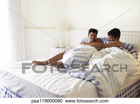 Stock Image - Two teenage boys playfighting in bed. Fotosearch