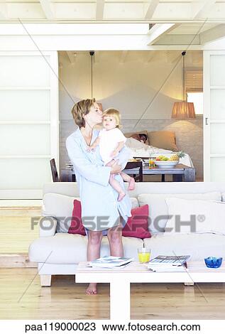 Stock Image - Woman holding baby, man sleeping in background. Fotosearch