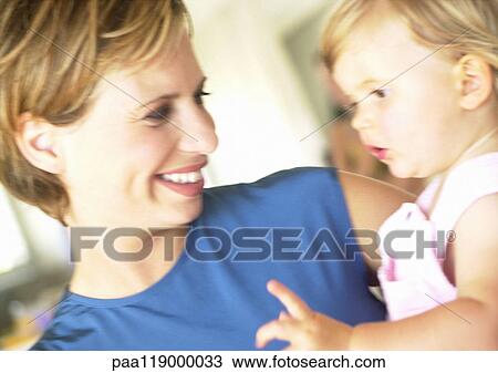 Stock Image - Woman holding baby, smiling, close-up. Fotosearch