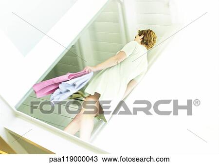 Stock Image - Woman walking with clothes in hand, low angle view. Fotosearch
