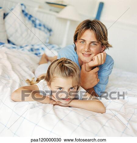Stock Image - Boy and girl lying on bed, looking at camera. Fotosearch