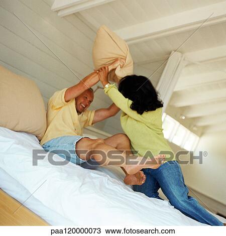 Stock Image - Couple having pillow fight on bed. Fotosearch