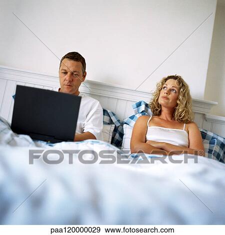 Couple in bed, man using laptop computer, woman with arms crossed View Large Photo Image Stock Photo - Couple in bed, man using laptop computer, woman with arms crossed. Fotosearch