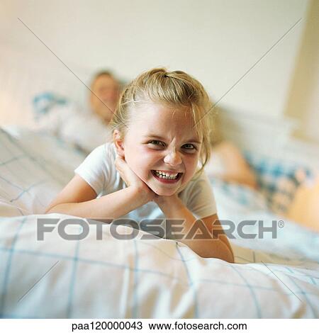 Girl lying at end of parent's bed, making face View Large Photo Image Stock Image - Girl lying at end of parent's bed, making face. Fotosearch