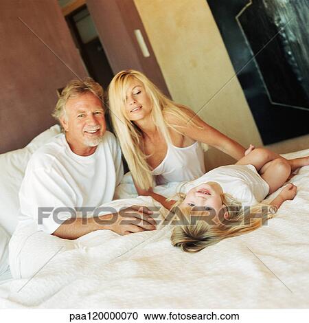 Girl lying on bed with parents View Large Photo Image Stock Image - Girl lying on bed with parents. Fotosearch
