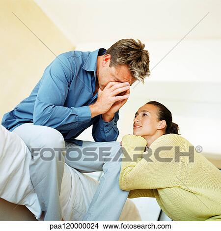 Picture - Man sitting on edge of bed with hands over face, woman leaning on his knee. Fotosearch
