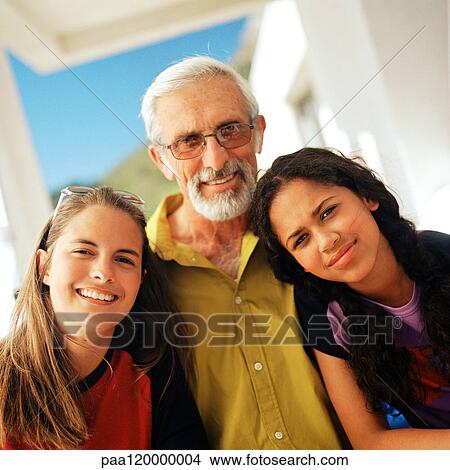 Picture - Senior man standing between two girls, smiling, portrait. Fotosearch
