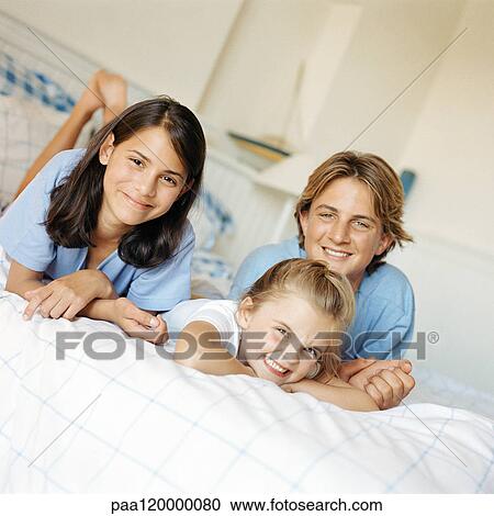 Stock Image - Three children lying on stomach on bed. Fotosearch