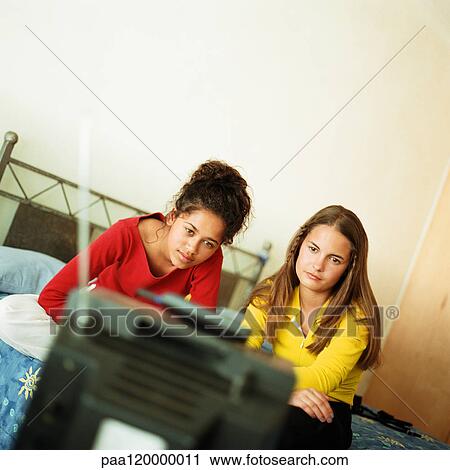 Stock Image - Two girls on bed watching television. Fotosearch