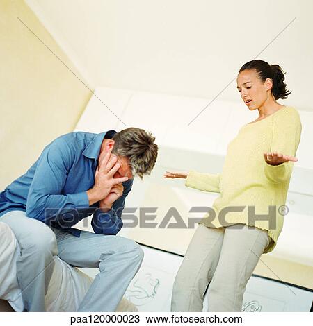 Woman standing, speaking and gesturing to man, man sitting with hands over face View Large Photo Image Stock Image - Woman standing, speaking and gesturing to man, man sitting with hands over face. Fotosearch