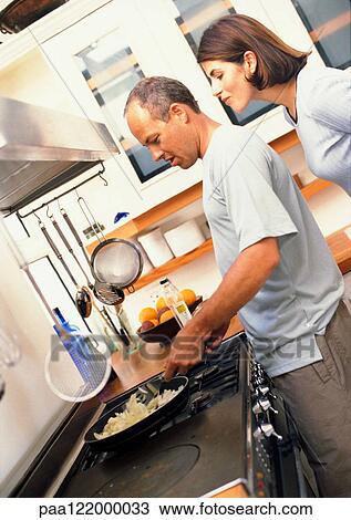 Couple in kitchen, man cooking while woman looks over his shoulder, side view View Large Photo Image Stock Image - Couple in kitchen, man cooking while woman looks over his shoulder, side view. Fotosearch