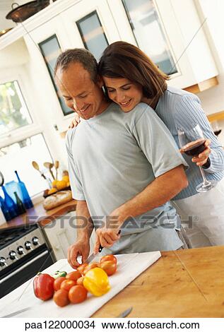 Couple in kitchen, man cutting vegetables while woman looks over man's shoulder View Large Photo Image Picture - Couple in kitchen, man cutting vegetables while woman looks over man's shoulder. Fotosearch