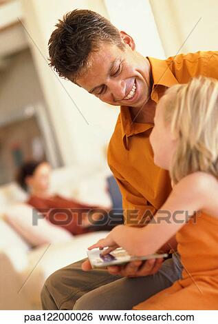 Father and daughter looking at book, smiling, woman sitting on sofa in background View Large Photo Image Stock Photograph - Father and daughter looking at book, smiling, woman sitting on sofa in background. Fotosearch