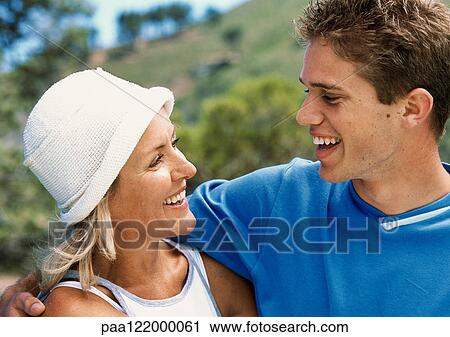 Stock Image - Teenage boy and mature woman smiling at each other, close-up. Fotosearch