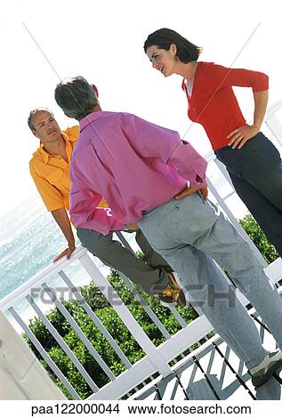 Two men and woman talking, sea in background View Large Photo Image Picture - Two men and woman talking, sea in background. Fotosearch