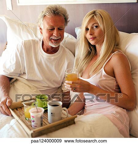 Couple sitting in bed, man holding tray of drinks View Large Photo Image Stock Photo - Couple sitting in bed, man holding tray of drinks. Fotosearch