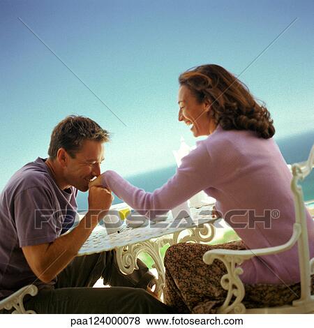 Stock Photo - Man kissing woman's hand, seated at table outdoors. Fotosearch