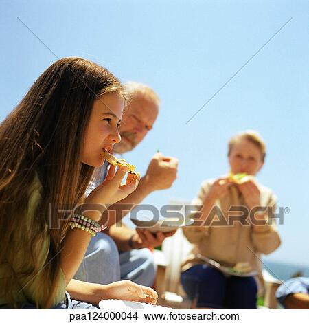 Mature couple and teenage girl eating outside, close-up View Large Photo Image Picture - Mature couple and teenage girl eating outside, close-up. Fotosearch