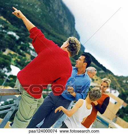People standing on deck, holding glasses, man leaning on railing and pointing View Large Photo Image Picture - People standing on deck, holding glasses, man leaning on railing and pointing. Fotosearch