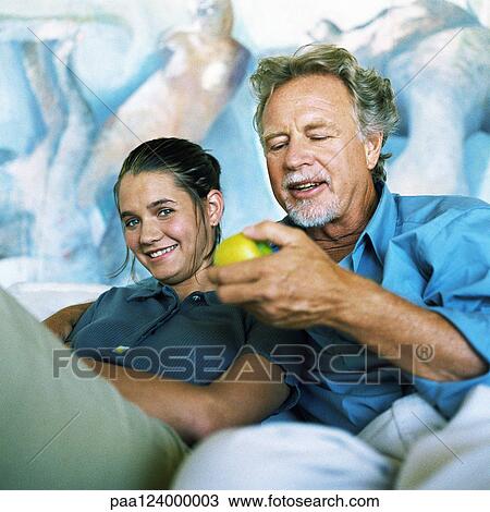 Stock Image - Teenage girl sitting with mature man holding fruit. Fotosearch