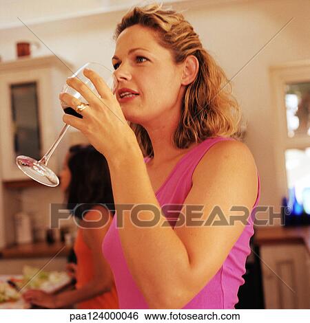 Stock Photograph - Woman drinking wine in kitchen, girl in background. Fotosearch