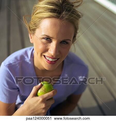 Stock Image - Woman holding apple, high angle view, portrait. Fotosearch