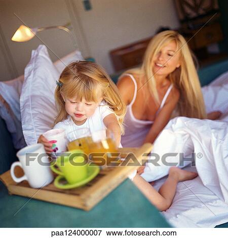 Woman sitting in bed, daughter reaching for glass from tray View Large Photo Image Stock Photo - Woman sitting in bed, daughter reaching for glass from tray. Fotosearch