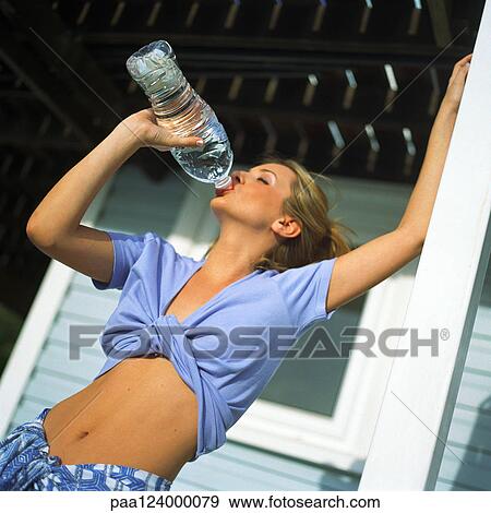 Young woman with bare midriff drinking from plastic bottle, low angle view View Large Photo Image Stock Photo - Young woman with bare midriff drinking from plastic bottle, low angle view. Fotosearch