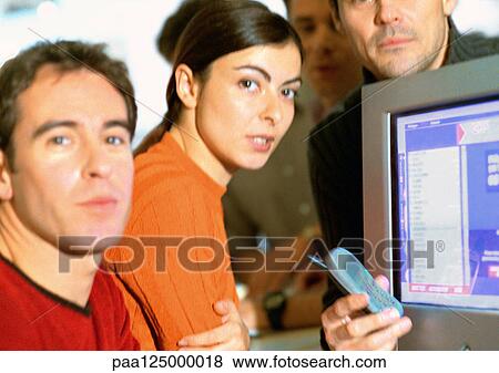 Stock Photo - Adults grouped around computer screen, close-up, looking at camera. Fotosearch
