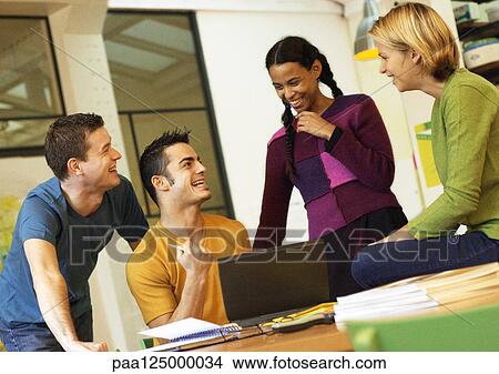 Four people smiling around desk with laptop computer View Large Photo Image Picture - Four people smiling around desk with laptop computer. Fotosearch