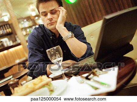 Picture - Man at cafe table, using laptop computer. Fotosearch