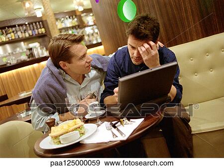 Two men at cafe table, one with laptop computer View Large Photo Image Stock Photo - Two men at cafe table, one with laptop computer. Fotosearch
