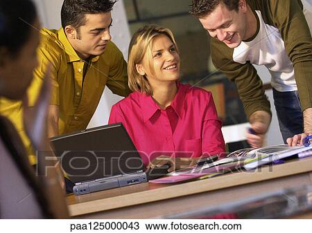 Stock Image - Two men behind woman using laptop computer. Fotosearch