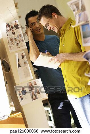 Two men smiling, one holding cell phone View Large Photo Image Stock Photograph - Two men smiling, one holding cell phone. Fotosearch