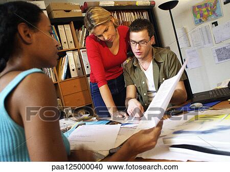 Two women and man at desk examining documents View Large Photo Image Stock Image - Two women and man at desk examining documents. Fotosearch